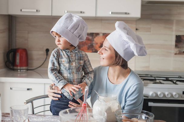 madre e hijo mirando hacia otro lado mientras preparan la masa en la cocina
 - Foto, Imagen