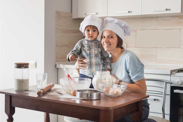 mother and child preparing dough at kitchen and looking at camera - Photo, Image