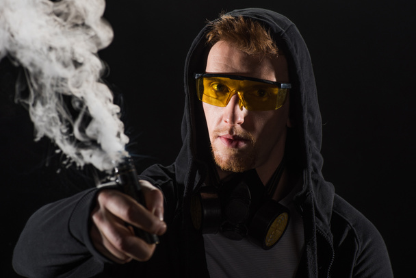 Man wearing protective filter mask activating electronic cigarette - Zdjęcie, obraz
