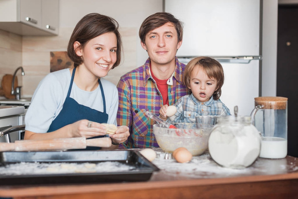 счастливая семья готовит тесто для домашнего печенья вместе и смотрит в камеру
 - Фото, изображение
