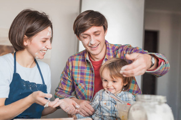 счастливые молодые родители и восхитительный маленький ребенок, играющий с полом на кухне
 - Фото, изображение