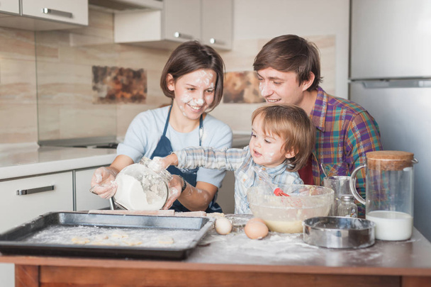 маленький ребенок помогает родителям с готовкой на кухне
 - Фото, изображение