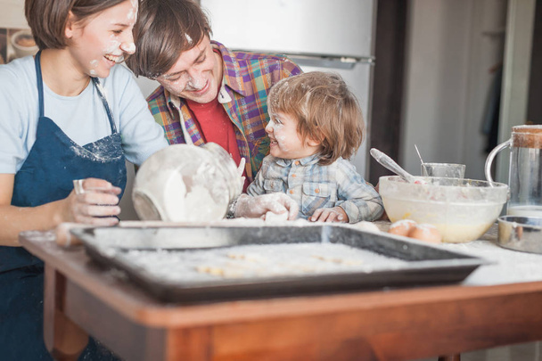 щаслива молода сім'я проливається борошном, проводячи час разом на кухні
 - Фото, зображення