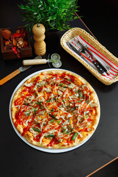 Vista próxima de deliciosa pizza italiana tradicional com linhas de molho de tomate, talheres, moedor de pimenta e plantador na superfície de madeira
. - Foto, Imagem