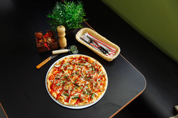 Delicious traditional italian pizza with cutlery, pepper grinder and green planter on wooden surface. - Photo, Image