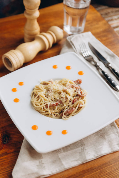 Close view of traditional italian pasta carbonara served on white plate with cuttery on napkin and pepper grinder. - Photo, Image