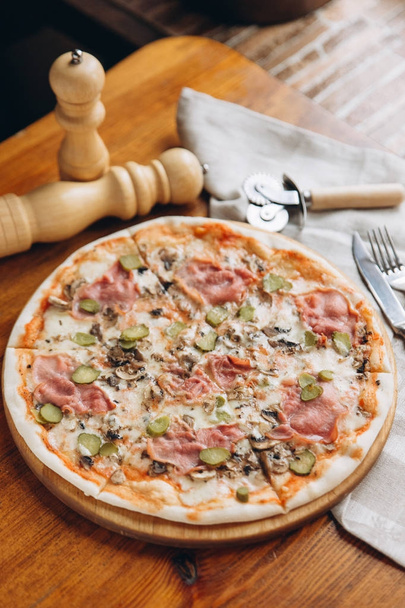 ízletes pizza a fa vágódeszka evőeszközök a vászon szalvéta és bors csiszolót a háttérben - Fotó, kép