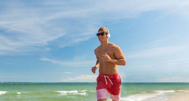 happy man with headphones running along beach - Fotó, kép