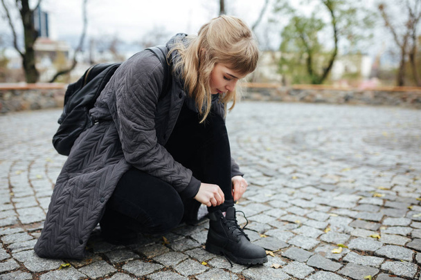 Foto de cerca de la hermosa chica con el pelo rubio doblado en la calle para atar los cordones de los zapatos aislados
 - Foto, imagen