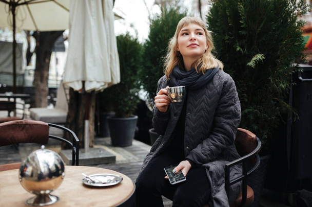 Close up photo of beautiful lady sitting at the table on street and drinking coffee isolated - 写真・画像