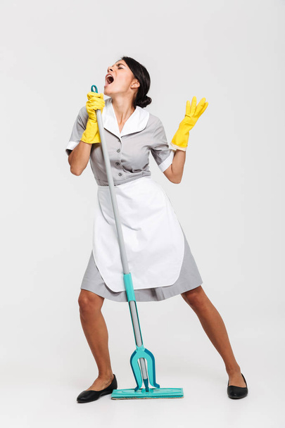 Full length portrait of funny housekeeper in uniform singing in  - Foto, immagini