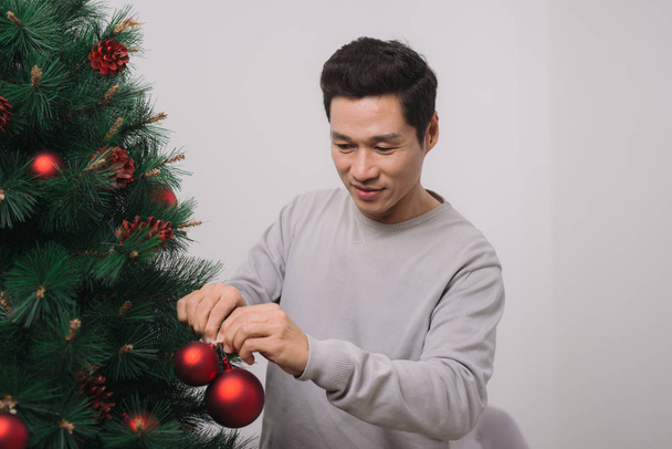  Asian man decorating Christmas tree at home  - Φωτογραφία, εικόνα