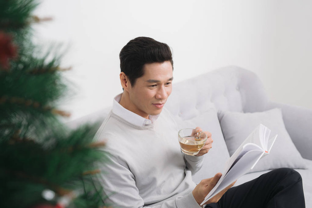 Ασιατικές άνθρωπος φορώντας πουλόβερ πίνοντας τσάι στο σπίτι κατά τη διάρκεια των Χριστουγέννων - Φωτογραφία, εικόνα