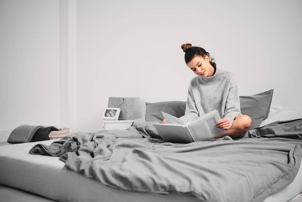 Женщина сидит на кровати по утрам и читает книгу
 - Фото, изображение