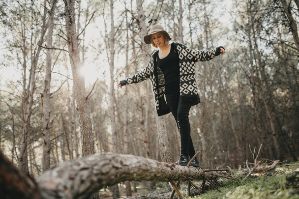 Woman in casual clothes walking on a fallen tree trunk in the forest - 写真・画像