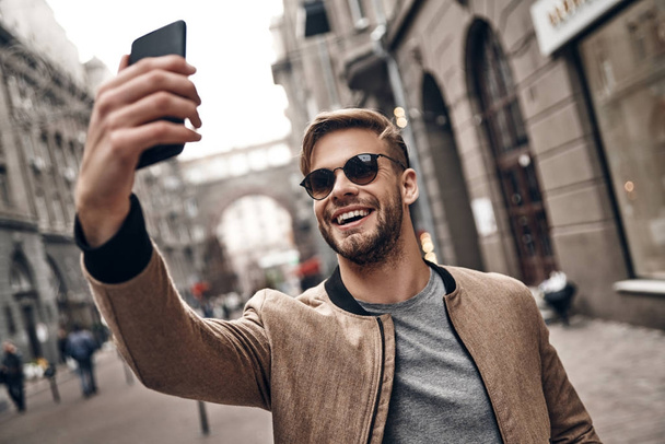 handsome young man in casual wear taking selfie on smartphone - Foto, imagen