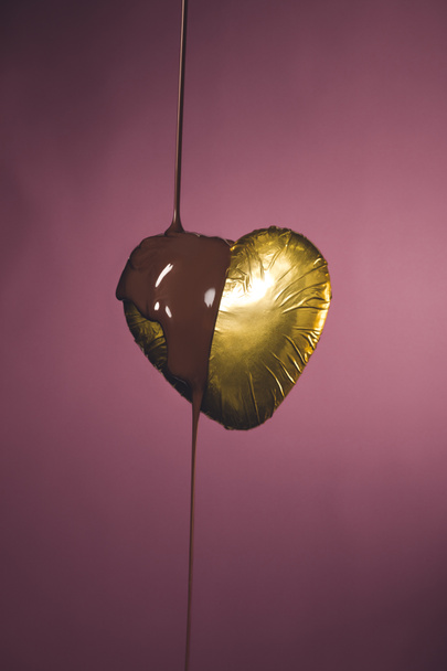 heart shaped candy in golden wrapper with liquid chocolate isolated on pink - 写真・画像