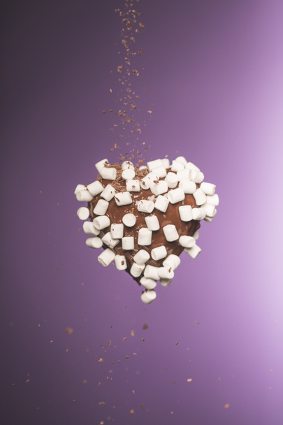 chocolate heart shaped candy with marshmallow and falling crumbled chocolate isolated on purple - Photo, Image