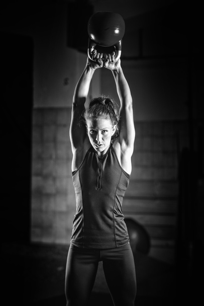 Женщина-спортсмен, занимающаяся спортом с гирями в помещении
 - Фото, изображение