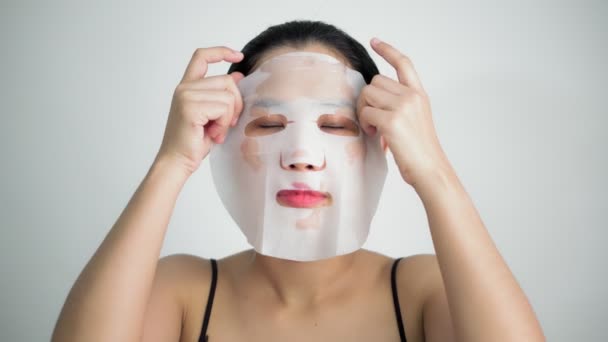 Mladá žena, která dělá maska listu s čistící maska na obličej na bílém pozadí - Záběry, video