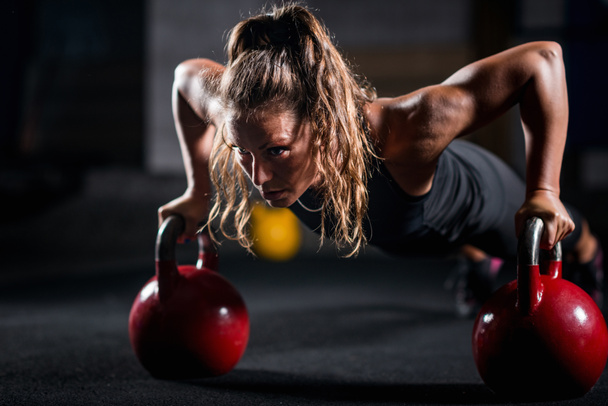 Woman athlete exercising with kettlebells indoors - Photo, Image