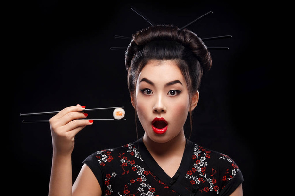 Mujer asiática sorprendida comiendo sushi y rollos sobre un fondo negro
. - Foto, imagen