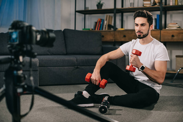 спортивний блогер сидить на підлозі і показує, як тренуватися з гантелями
 - Фото, зображення