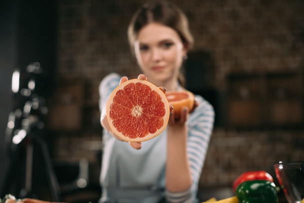 молодой блогер показывает половину грейпфрута на камеру
 - Фото, изображение