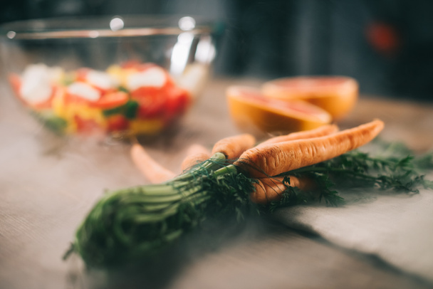 ripe carrots on wooden table with vegetables on blurred background - Foto, imagen
