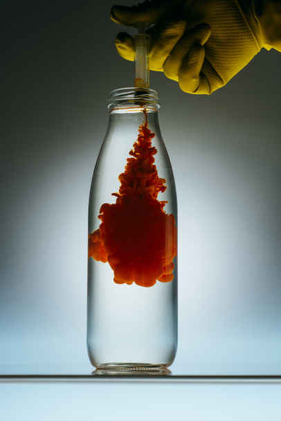 vista recortada de la persona que vierte pintura roja de la jeringa en botella con agua
 - Foto, imagen
