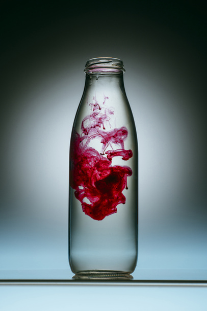 close up view of pink paint splash in bottle of water - 写真・画像