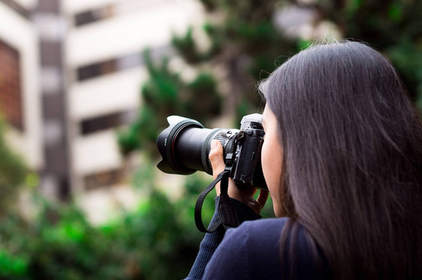 junge Frau, die mit ihrer Kamera pirscht und fotografiert, draußen mit Bürohintergrund - Foto, Bild