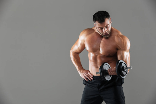 Portrait of a serious strong shirtless male bodybuilder lifting - Fotoğraf, Görsel