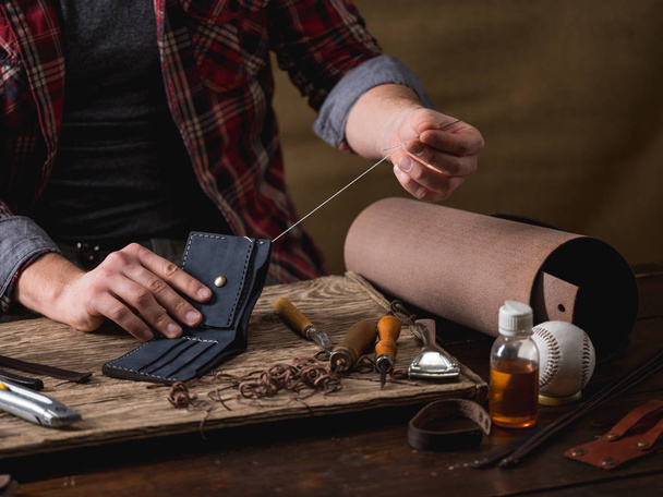 close-up of male hands sew leather wallet on wooden table - Foto, Imagen