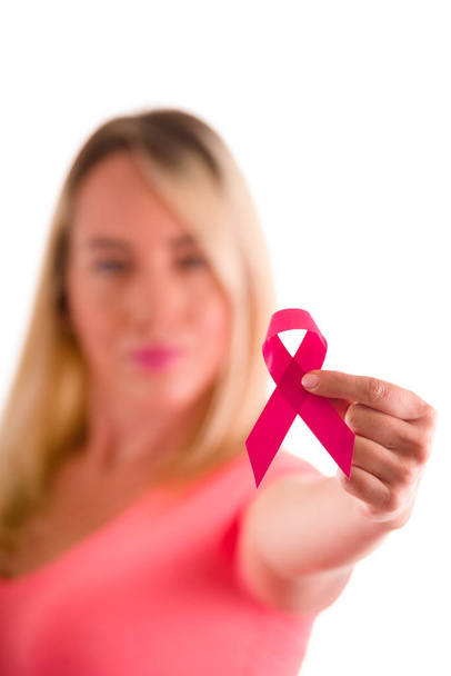 Blurred woman wearing a pink blouse pointing in front of her a pink ribbon, healthcare and medicine concept in a white background - Photo, Image