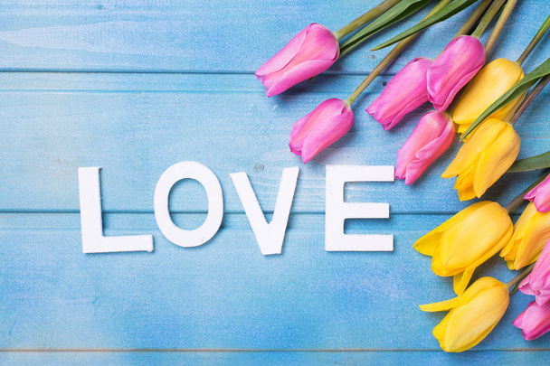 Word love and pink, yellow and white flowers on blue wooden background. Love concept.  - Foto, afbeelding