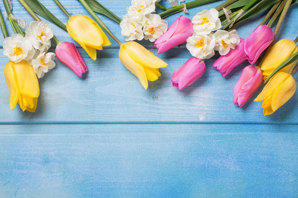 Border from yellow tulips and daffodils on blue wooden background - Foto, imagen