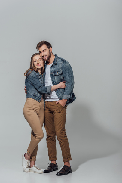full length view of cheerful young couple hugging and smiling at camera isolated on grey - Photo, image