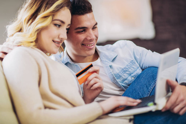 Młoda para szczęśliwy, siedząc w domu za pomocą laptopa i kartą kredytową za zakupy online  - Zdjęcie, obraz