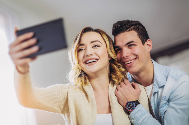 young happy couple sitting on couch at home and looking at digital tablet - Photo, Image