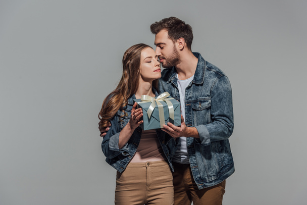 guapo joven besando novia y presentando caja de regalo aislado en gris
 - Foto, imagen