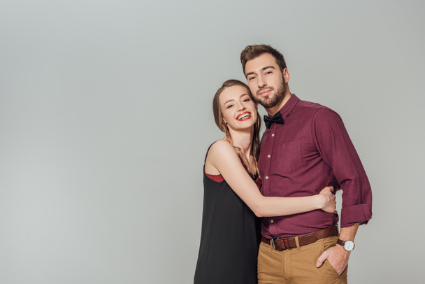 elegant young couple hugging and smiling at camera isolated on grey - Foto, Imagem