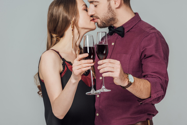 close-up vista de belo jovem casal segurando copos de vinho tinto e beijando isolado em cinza
  - Foto, Imagem