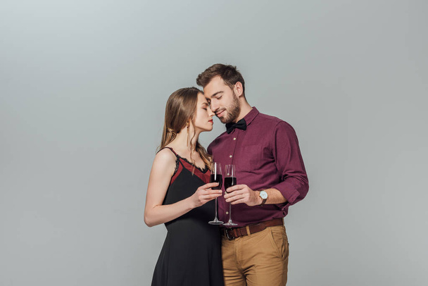 beautiful fashionable young couple holding glasses of red wine isolated on grey - Foto, Imagen
