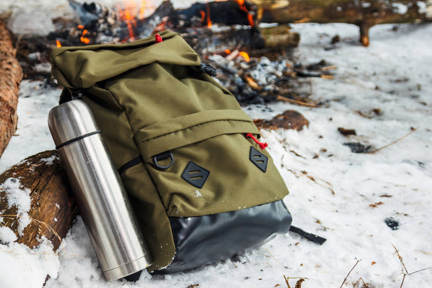 Backpack in the background of a burning bonfire in the winter forest. Green backpack. - Photo, Image
