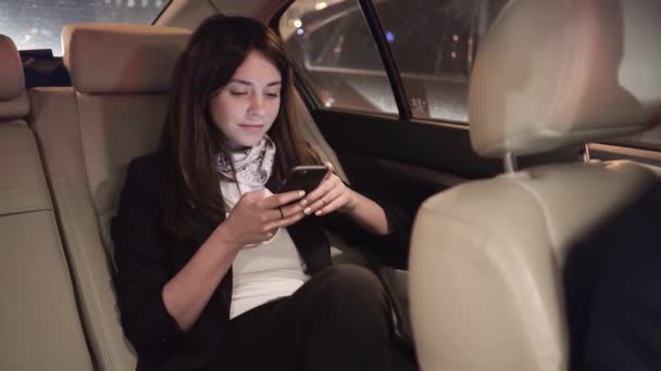 Businesswoman smiling while looking at her smartphone in a car - Кадры, видео