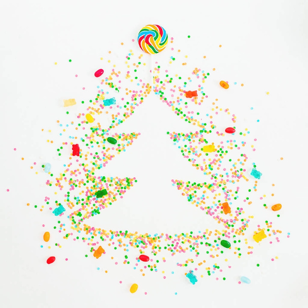 Árbol de Navidad hecho de colorido confeti brillante, mermelada y caramelo arco iris sobre fondo blanco. Piso tendido, vista superior
 - Foto, imagen