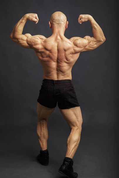 Αθλητής στην πλάτη διπλά δικέφαλου πόζα. Bodybuilder που δείχνει τους μυς στο ιστορικό στούντιο - Φωτογραφία, εικόνα