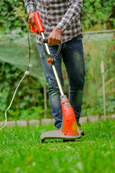 Young worker using a lawn trimmer mower cutting grass in a blurred nature background - Foto, imagen