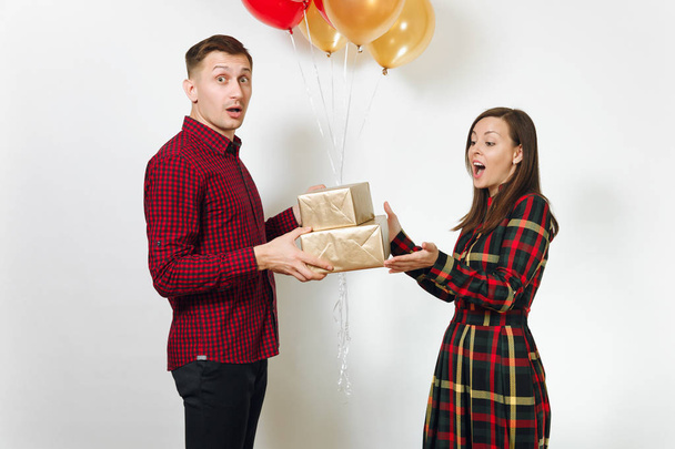 Beautiful young happy smiling couple in love. Woman and man holding golden gift boxes with present and red, yellow balloons, celebrating birthday, on white background isolated. Holiday, party concept. - Fotoğraf, Görsel